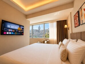 A hotel room with a large bed, a TV mounted on the wall, a window with a city view, and a lamp on the nightstand. - The Tram Karakoy (İstanbul)