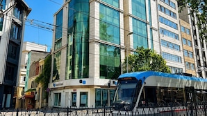 A modern building with large glass windows, a sign for 'Anadolu Bank,' and a tram in the foreground. - The Tram Karakoy (İstanbul)