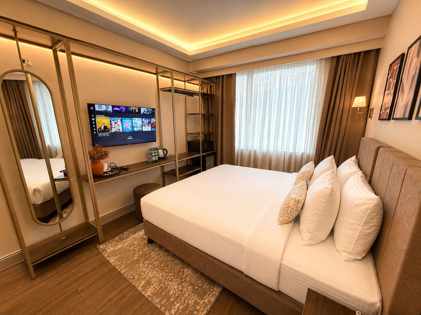 Une chambre d’hôtel moderne avec un grand lit, un téléviseur fixé au mur, un bureau avec un miroir et une fenêtre avec des rideaux.