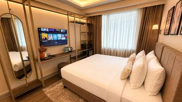 Une chambre d’hôtel moderne avec un grand lit, un téléviseur fixé au mur, un bureau avec un miroir et une fenêtre avec des rideaux.