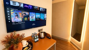 A flat-screen TV mounted on a wall displaying various streaming content, a coffee table with a tray of items, and a potted plant. - The Tram Karakoy (İstanbul)