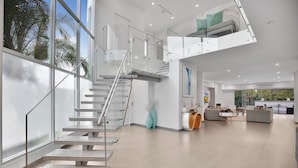 Ein modernes Interieur mit einer Glasstiege, einer Wohnbereits mit Sofas und einem Essbereich.