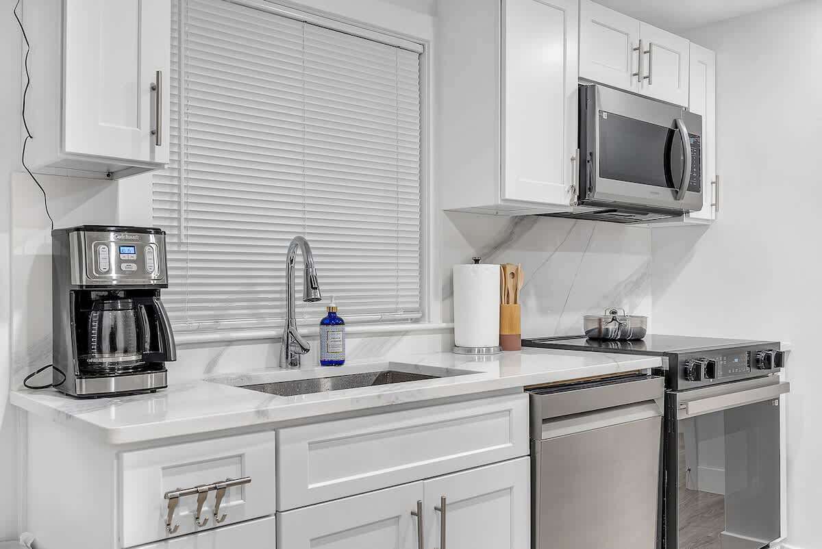 Una cocina moderna con armarios blancos, una cafetera de acero inoxidable, microondas y lavavajillas.