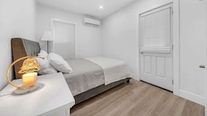 Ein Schlafzimmer mit Bett, Nachttisch, Lampe und einem Fenster mit Jalousien.