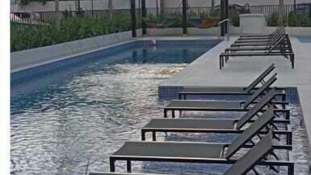 Ein Schwimmbecken mit Liegestühlen und einer Pergola, umgeben von Grünpflanzen und einem Berg im Hintergrund.