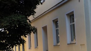Un bâtiment à la façade symétrique, doté de nombreuses fenêtres, avec un arbre au premier plan.