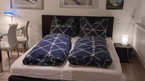 Un letto rifatto con cura, con copriletto e cuscini a motivi blu e bianchi, un comodino con una lampada e quadri appesi alla parete.