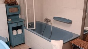Un bagno con una vasca blu, uno scaffale in legno con asciugamani e una sedia in vimini.