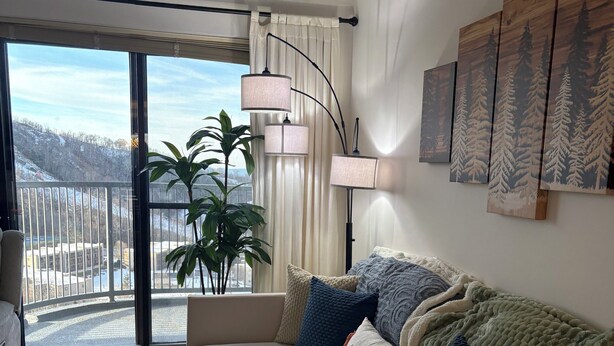 Et moderne soveværelse med en stor seng, udsigt til et sneklædt landskab gennem en skydedør, en potteplante og en vægmonteret lampe.