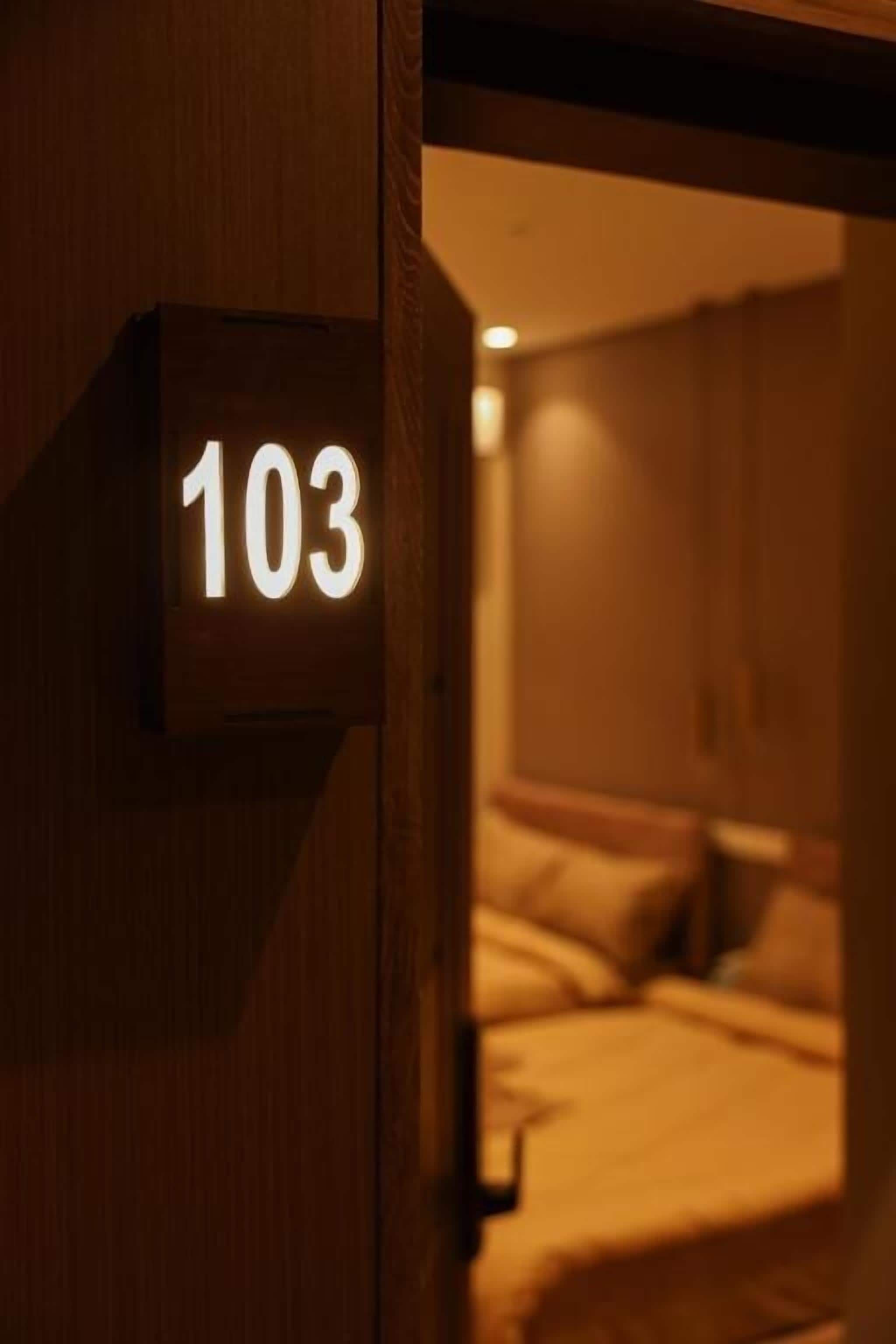 A wooden door with a lit number '103' sign, indicating a room number.