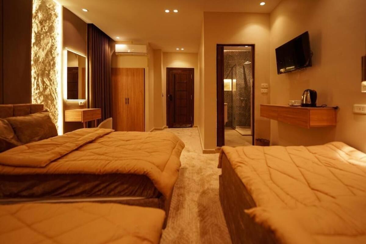 Une chambre d’hôtel avec deux lits, un téléviseur fixé au mur, une armoire en bois et une salle de bain visible à travers une porte ouverte.