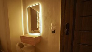 Une chambre comprenant une table de chevet, une chaise, un miroir avec éclairage et une porte dotée d’une serrure.
