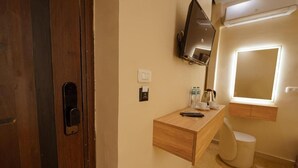 Une salle de bain avec un meuble-lavabo en bois, un miroir, des toilettes et un téléviseur fixé au mur.