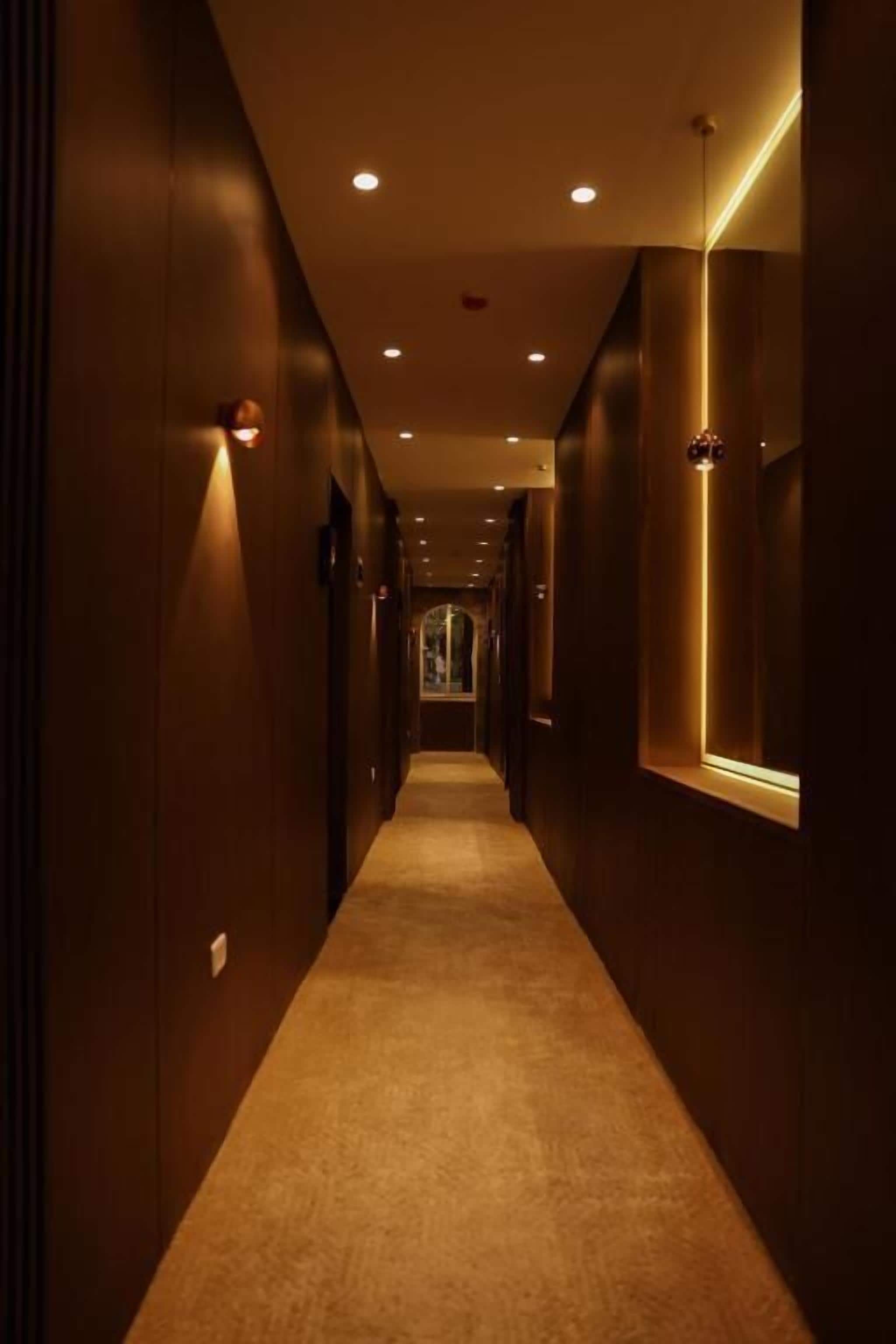 Un pasillo estrecho y tenuemente iluminado, con paredes de madera y suelo alfombrado, que conduce a una puerta al final.
