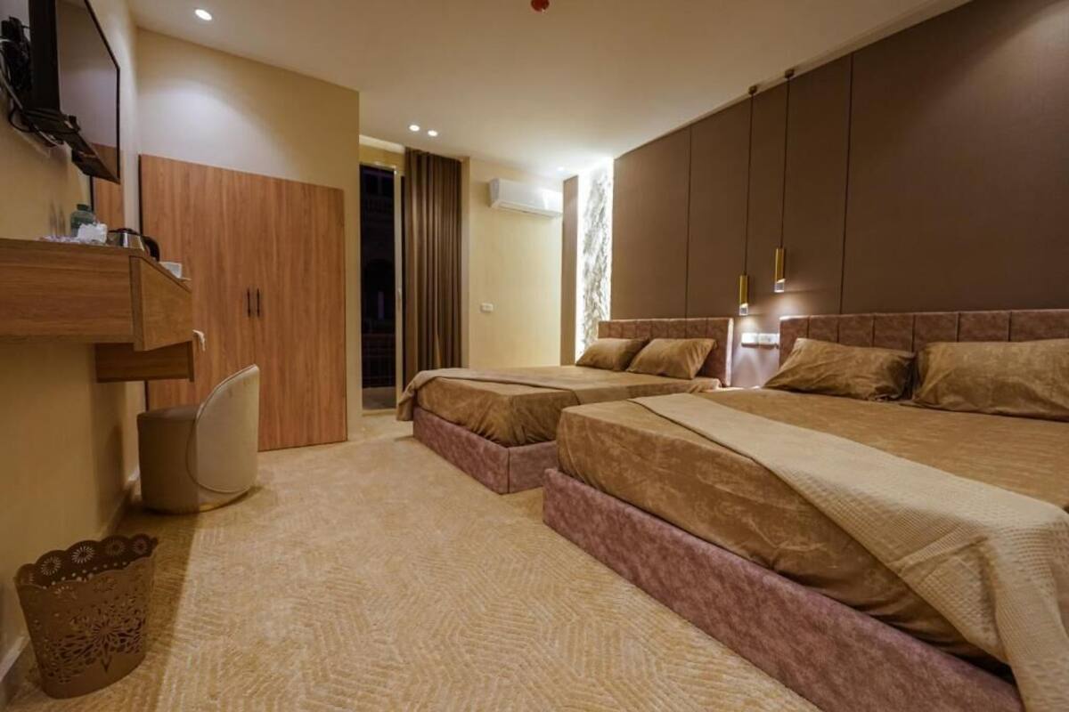 Une chambre d’hôtel avec deux lits, une armoire en bois, un petit coin salon et une poubelle.