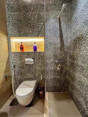 A compact bathroom with a toilet, a shower area, and a shelf with toiletries. - Sydney Hotel (Cairo)