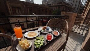 Un balcon avec un plateau contenant divers éléments pour le petit-déjeuner, notamment des fruits coupés, un verre de jus d’orange et une assiette d’œufs.
