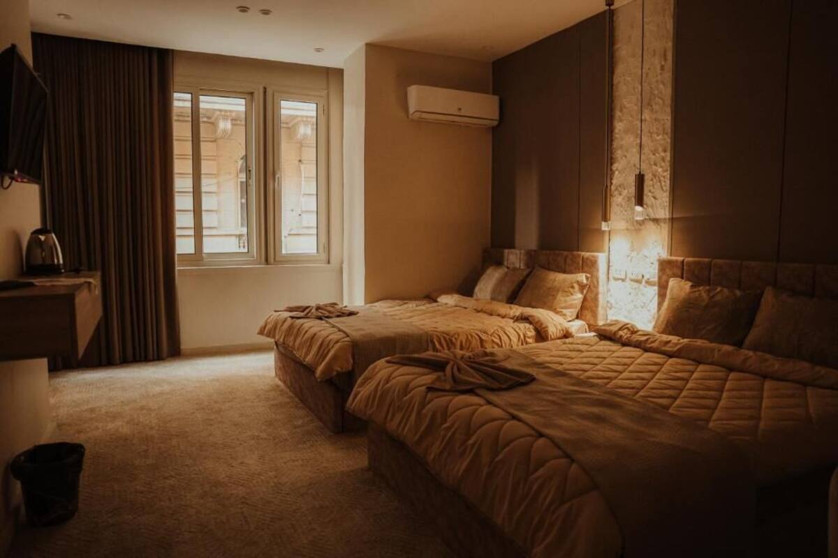Une chambre d’hôtel avec deux lits, une grande fenêtre, un climatiseur et un téléviseur posé sur un meuble.
