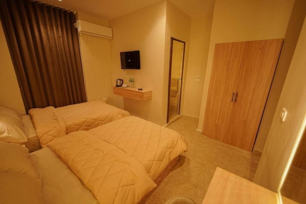 Une chambre d’hôtel avec deux lits, une télévision, une petite table avec une bouilloire et une armoire.