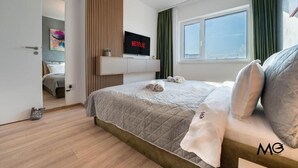 A modern hotel room with a large bed, a TV on the wall, and a view of the city. - MoHost Arena (Brașov)