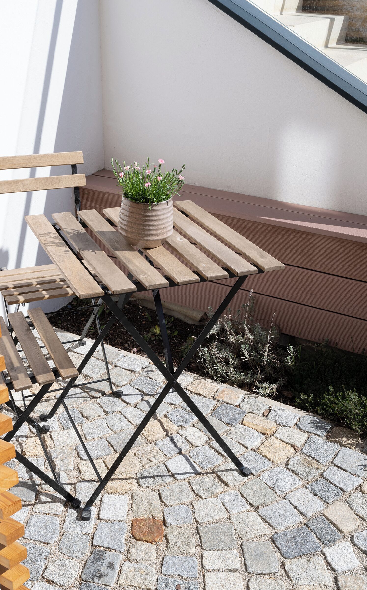 An outdoor wooden table with a potted plant, set on a stone-paved patio.