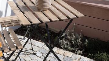 An outdoor wooden table with a potted plant, set on a stone-paved patio.