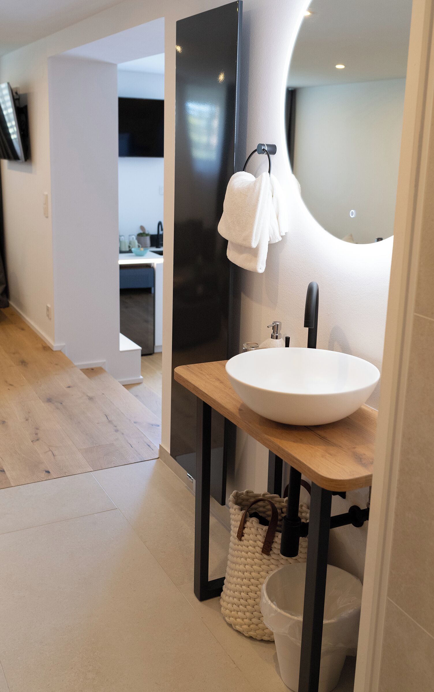 A modern bathroom with a large mirror, a white sink, and a wooden vanity.