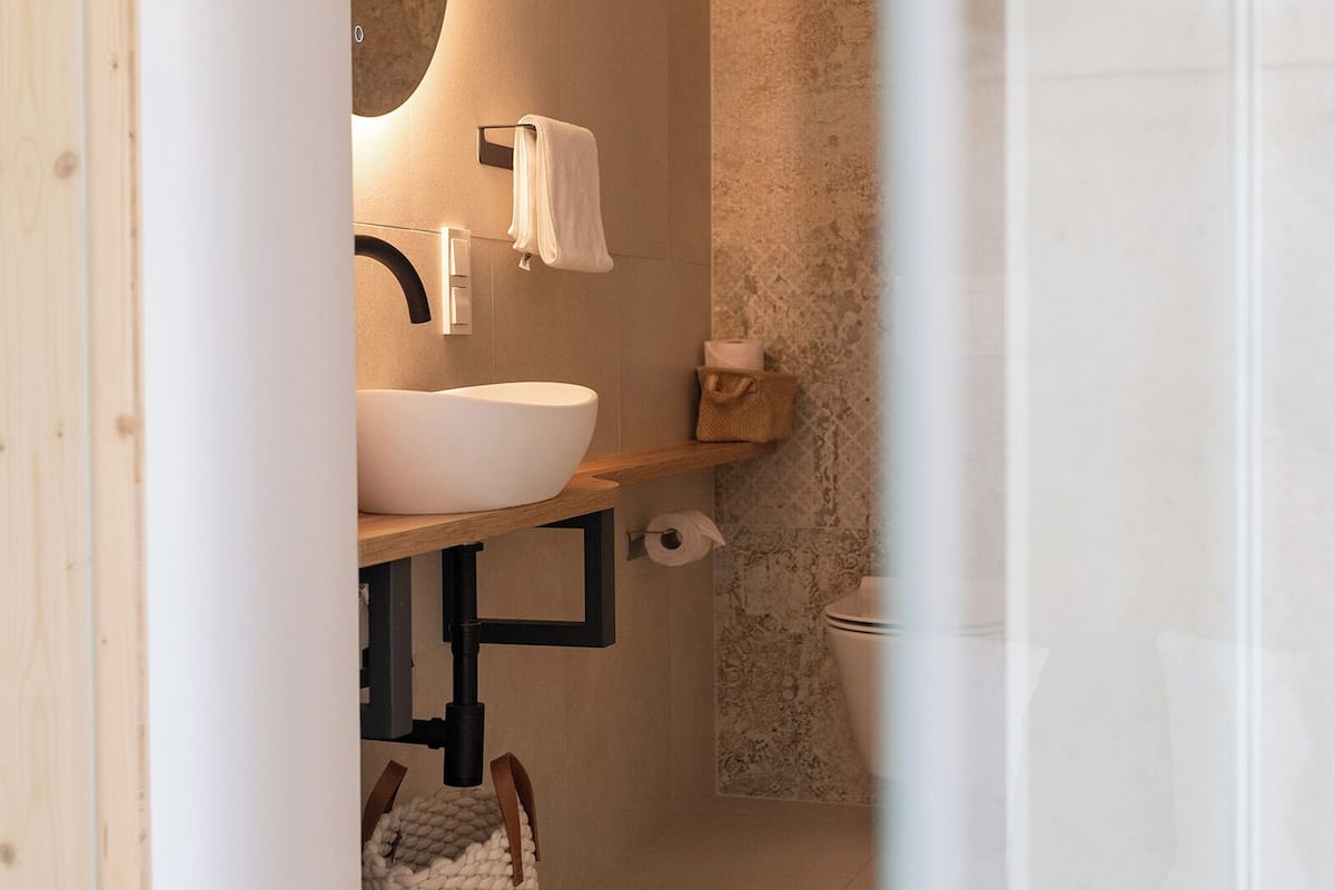 Un baño moderno con un lavabo blanco grande, un espejo redondo y una toalla colgada en la pared.