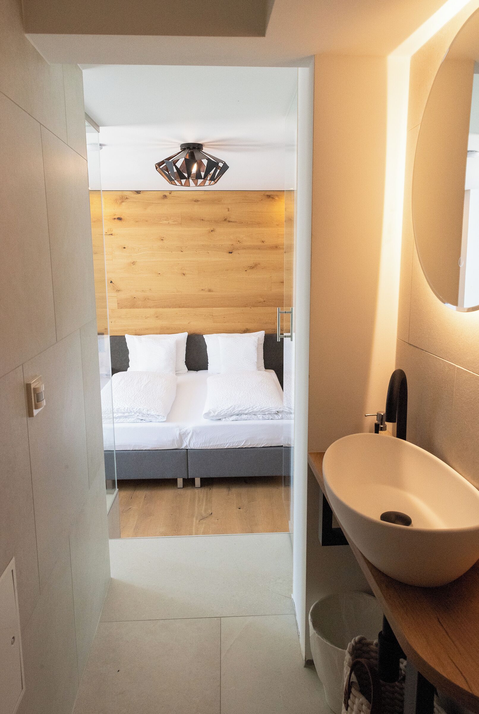 Une chambre moderne avec une tête de lit en bois, un grand lit, une table de chevet avec un lavabo blanc et un ventilateur de plafond.