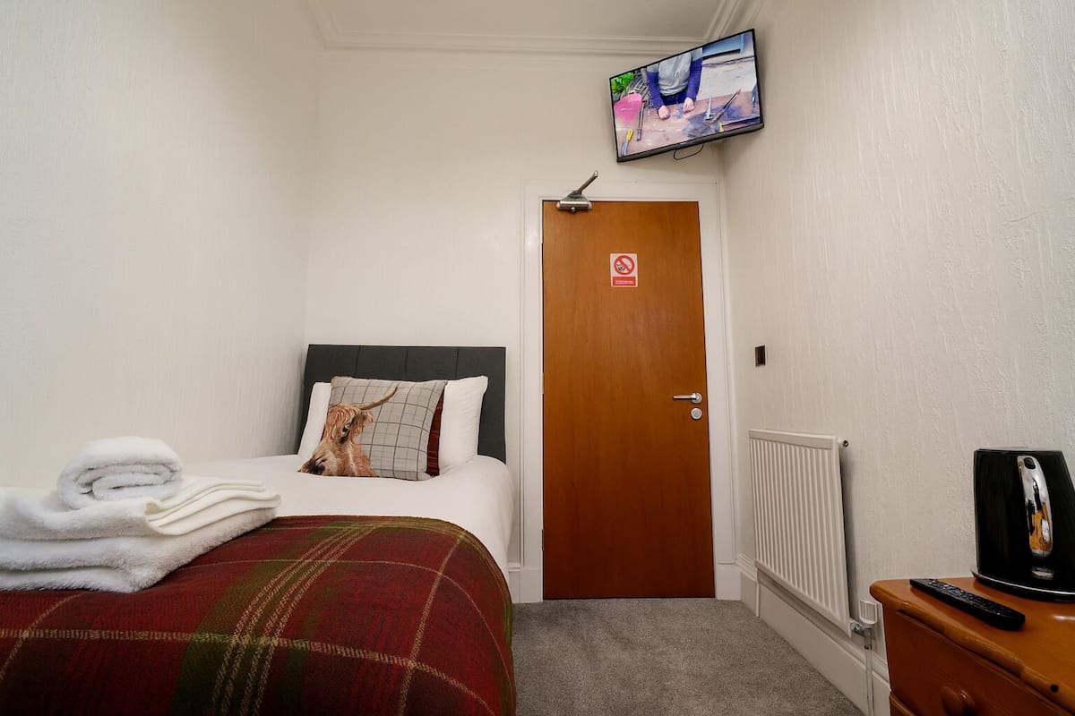 Una habitación de hotel con cama, televisor montado en la pared, puerta con letrero de no fumar y radiador.