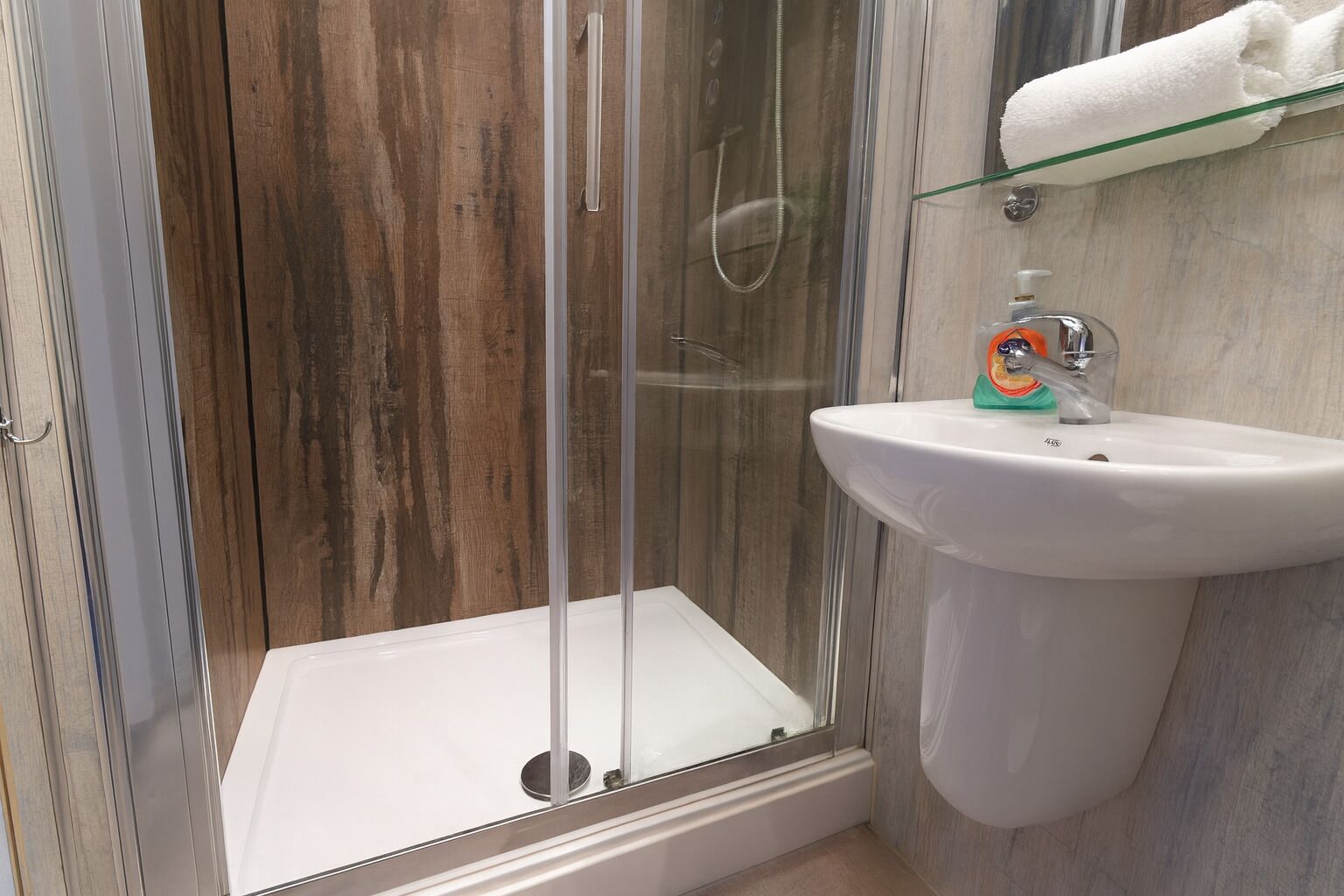 A modern bathroom with a glass shower enclosure, a white pedestal sink, and a wooden vanity.