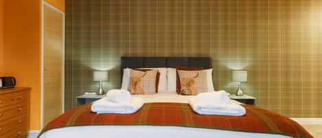 A hotel room with a bed, two nightstands, a lamp, a dresser, and a plaid-patterned wall.