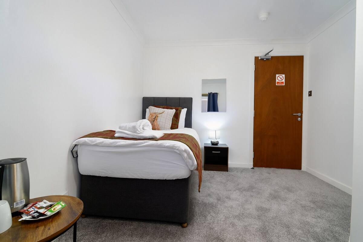 Una habitación de hotel con cama, mesita de noche y una puerta.