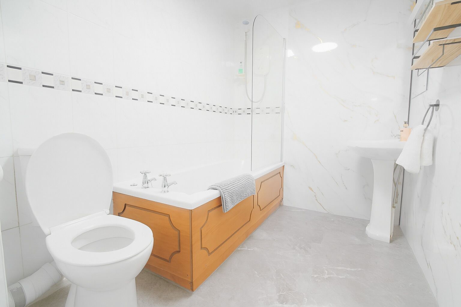 A modern bathroom with a toilet, wooden vanity, and a marble sink.