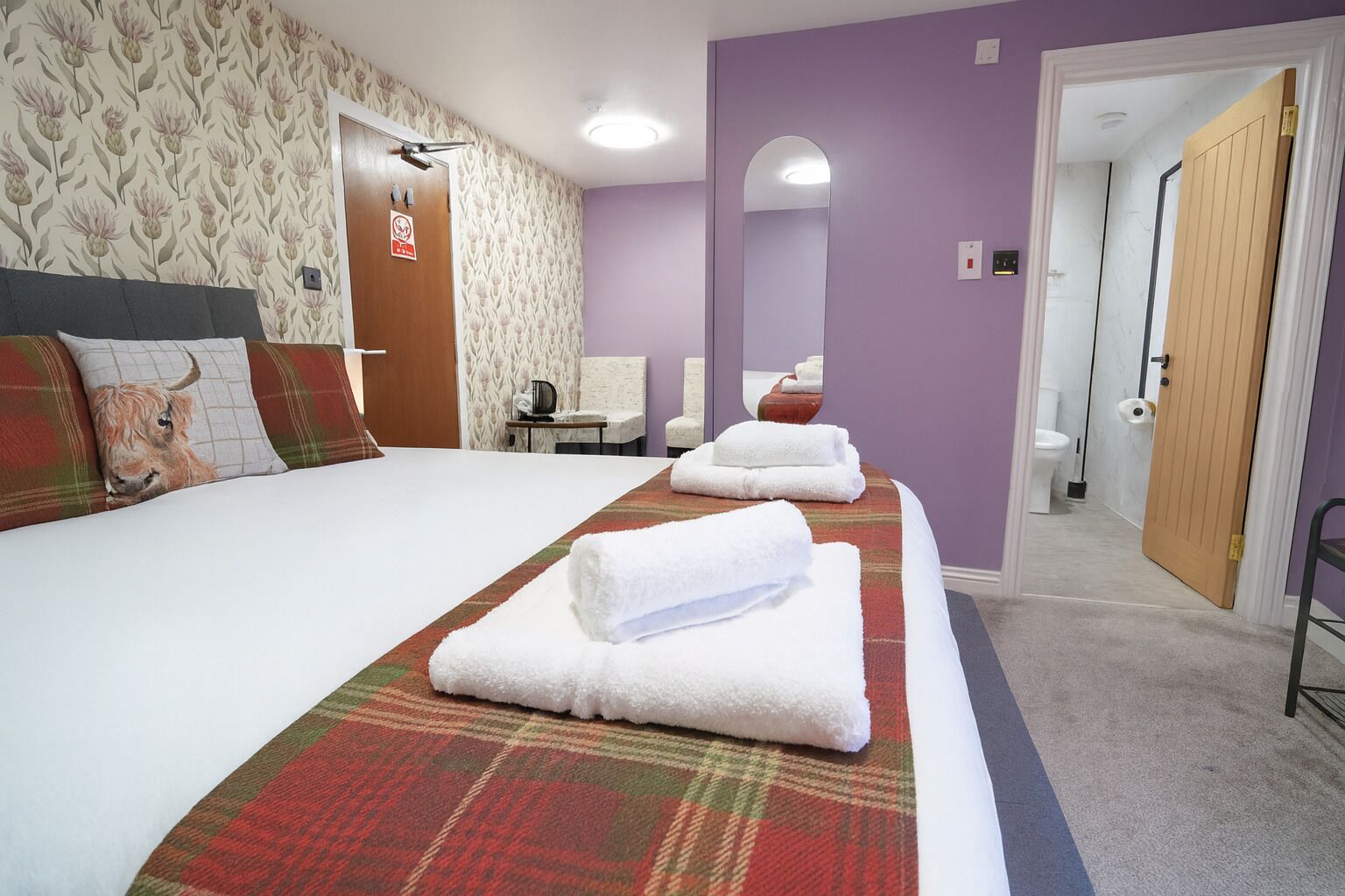 A hotel room with a bed, a mirror, a door, and a bathroom visible through an open door.