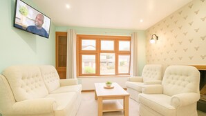 Ein Wohnzimmer mit zwei beige Sofas, einem Holztisch und einem an der Wand befestigten Fernseher.