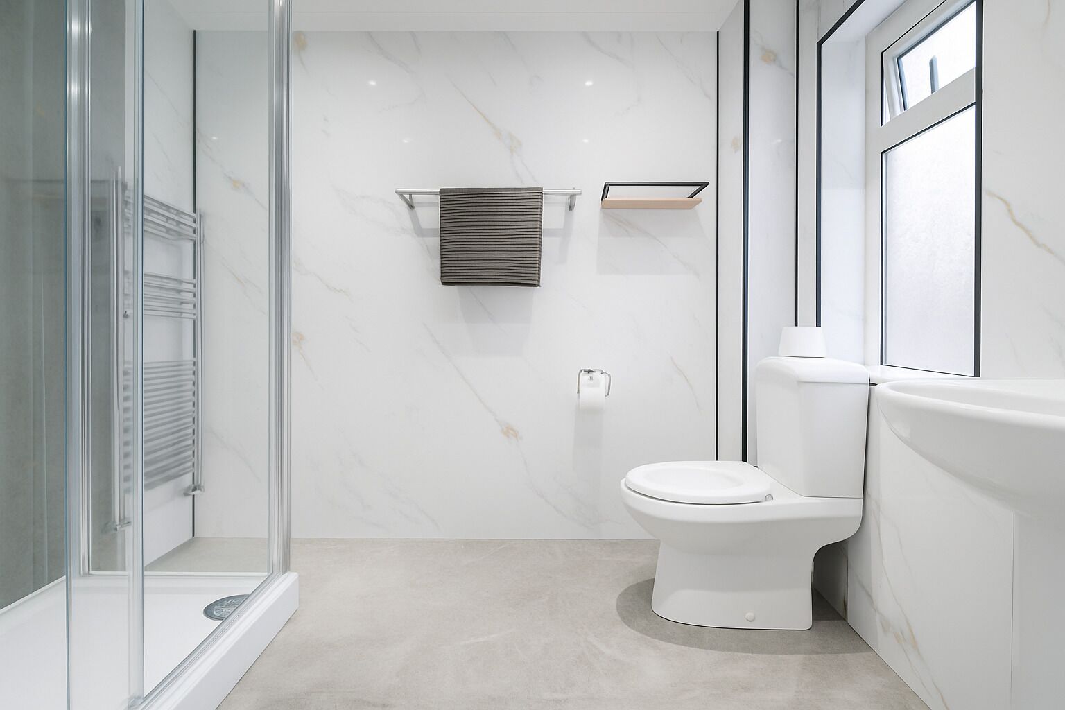 Un baño moderno con cabina de ducha de cristal, inodoro blanco y pared de mármol.