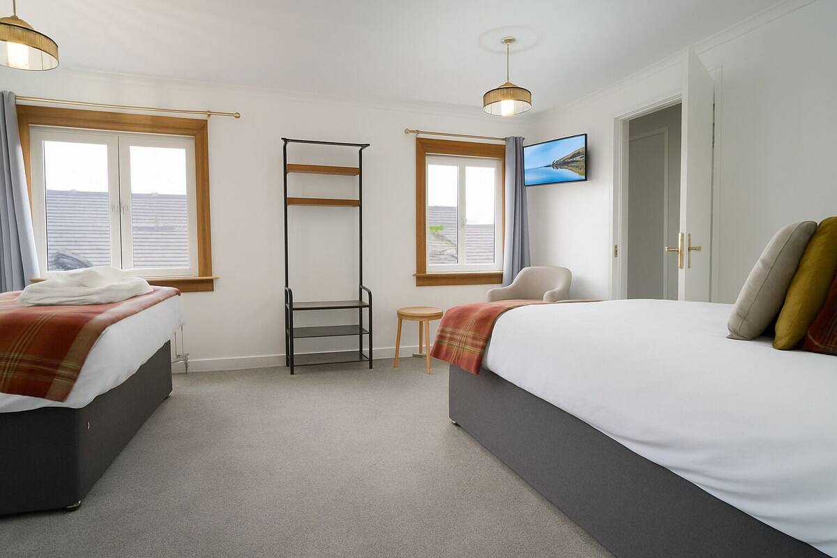 Habitación de hotel con dos camas, una mesita, una silla, una escalera y un televisor en la pared.