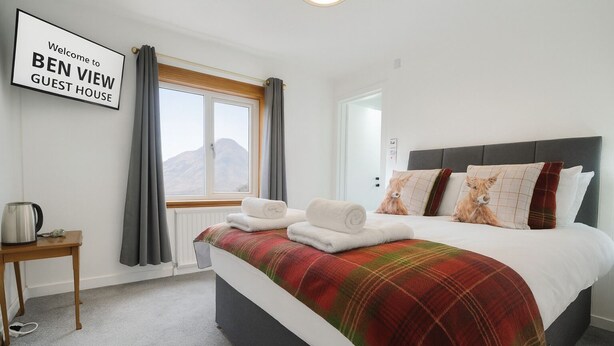 Ein Gästezimmer mit einem Bett, einem Nachttisch mit Wasserkocher, einem Fenster mit Vorhängen und einem Schild mit der Aufschrift 'Welcome to BEN VIEW GUEST HOUSE'.