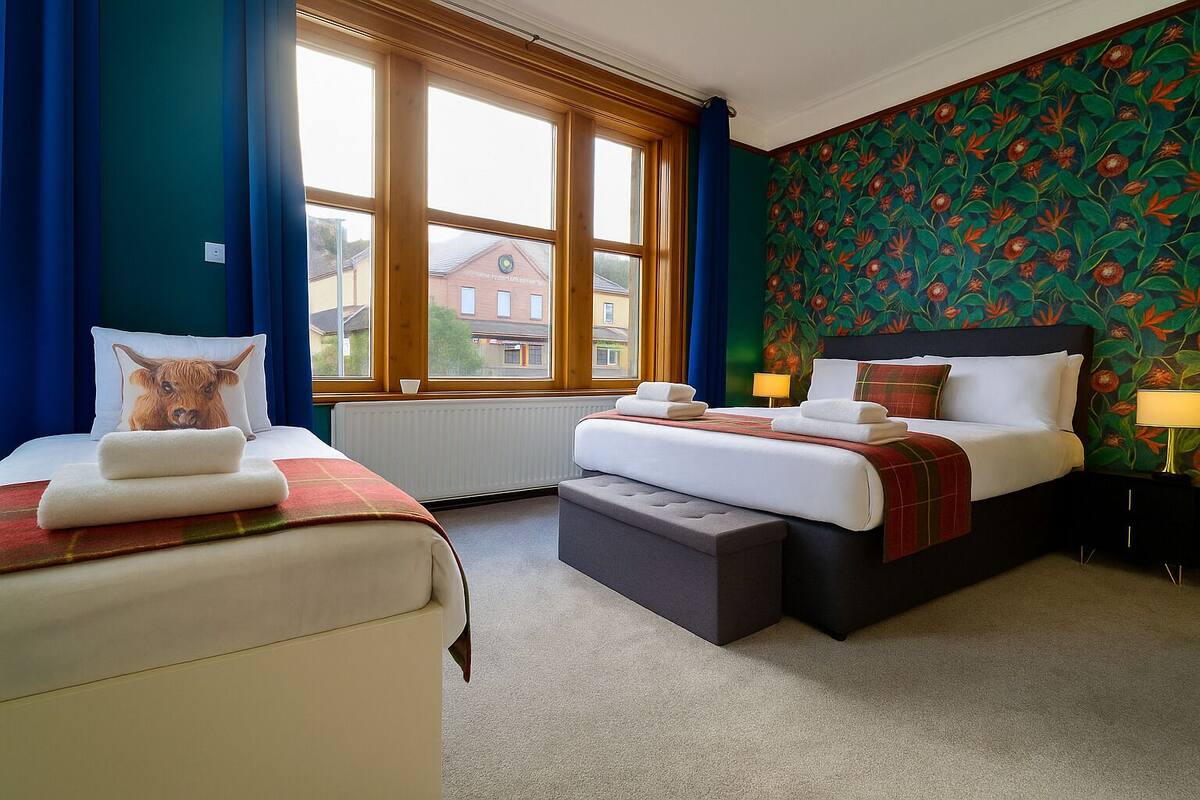 Habitación de hotel con dos camas, un ventanal grande y papel tapiz floral.