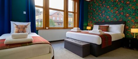Habitación de hotel con dos camas, un ventanal grande y papel tapiz floral.
