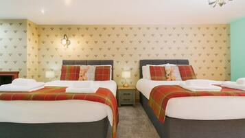 A hotel room with two beds, each with a plaid bedspread and matching pillows. There are bedside tables with lamps, a chandelier, and a patterned wallpaper.