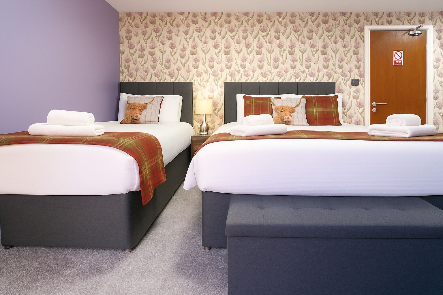 Una habitación de hotel con dos camas, cada una con cabecera, mesita de noche y lámpara.