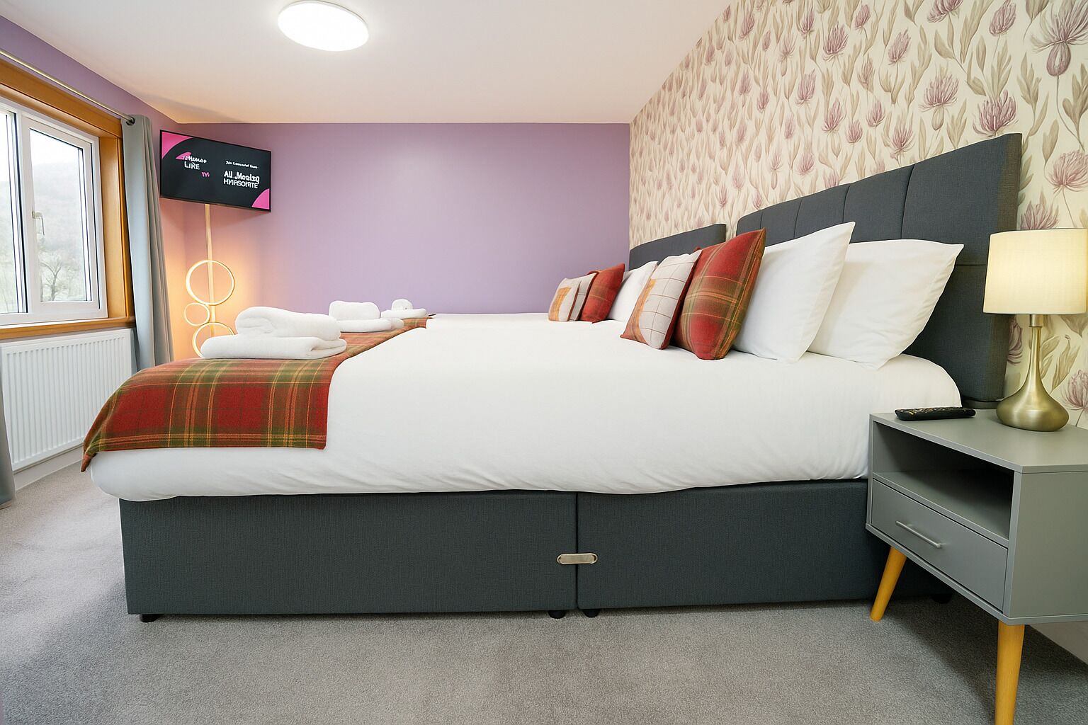 A modern bedroom with a large bed, a television on the wall, and a nightstand with a lamp.