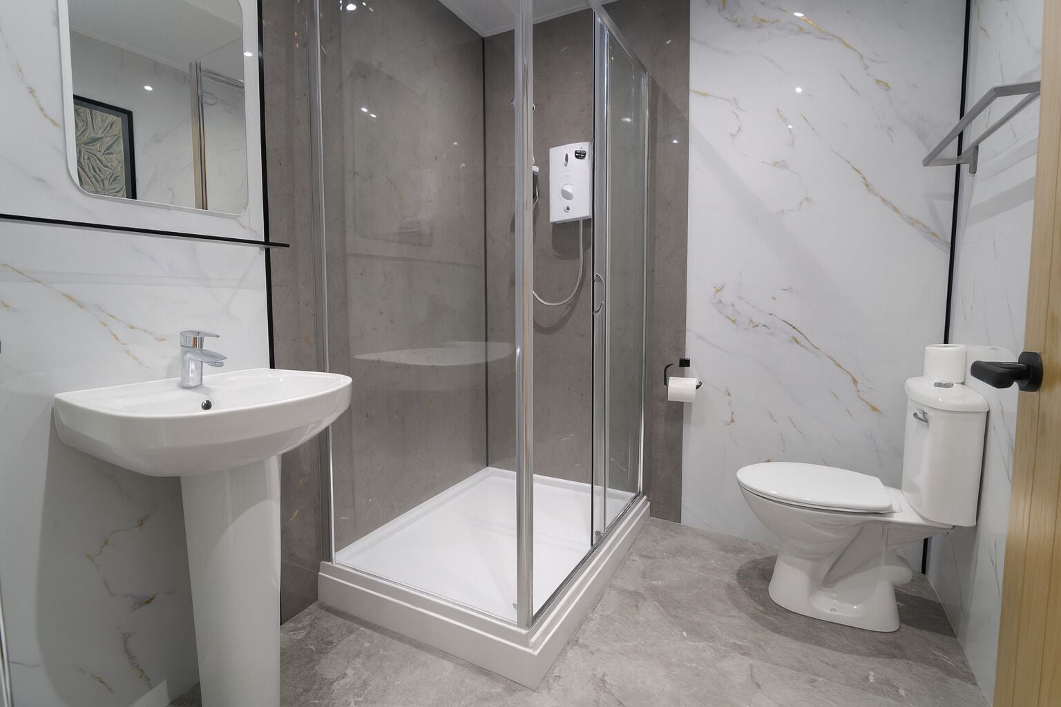 A modern bathroom with a glass-enclosed shower, a pedestal sink, and a toilet.