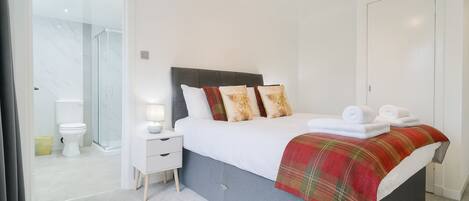 A hotel room with a bed, a bedside table with a lamp, a bathroom with a toilet and shower, and a wardrobe.