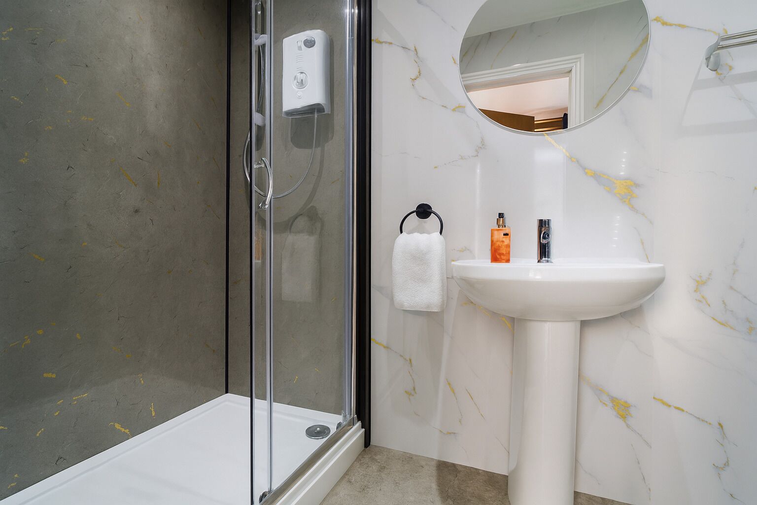 Un baño con cabina de ducha de vidrio, un lavabo blanco y un salpicadero de mármol.