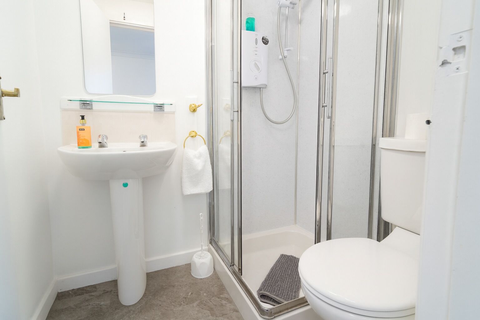 A modern bathroom with a glass-enclosed shower, a pedestal sink, and a toilet.