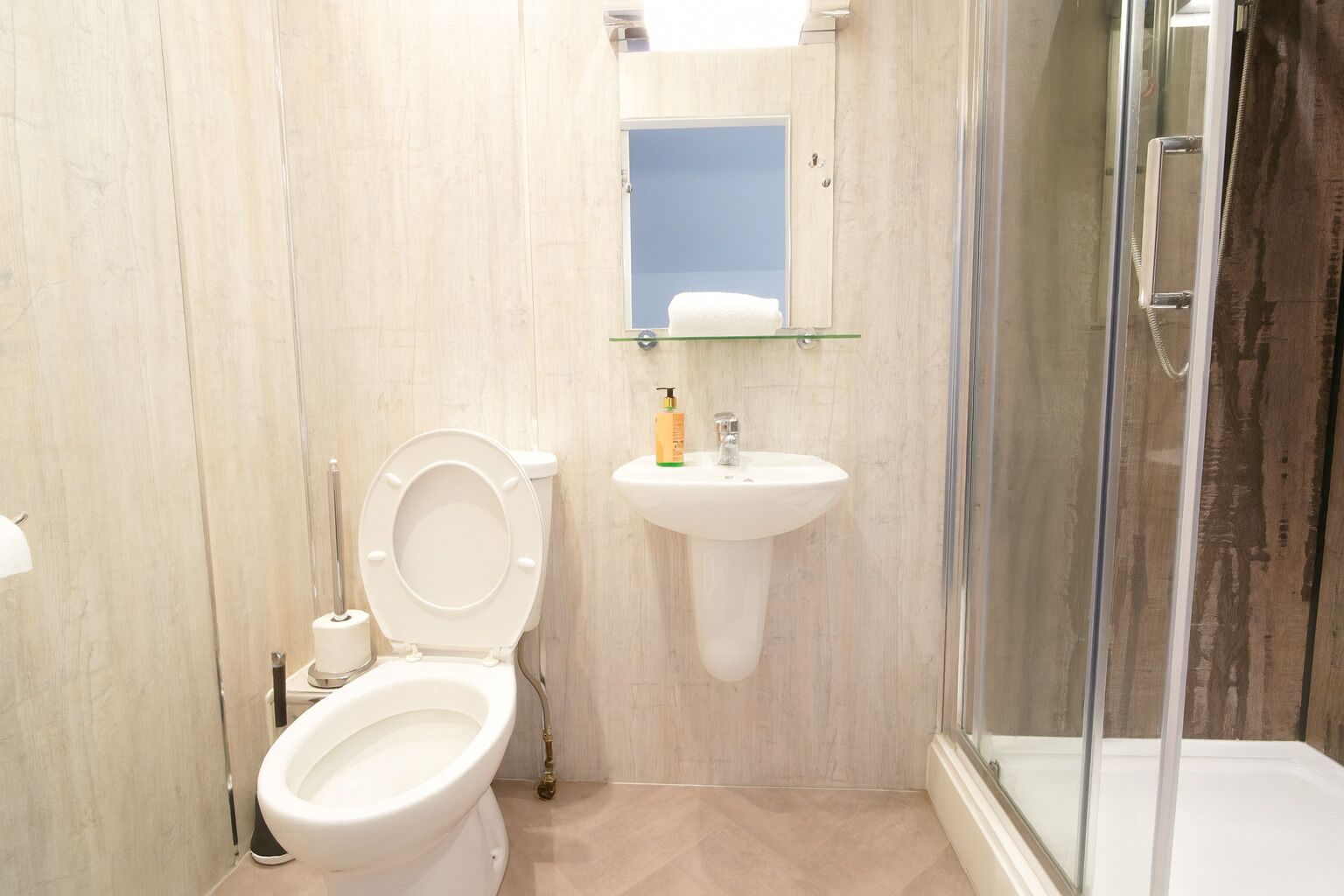 A bathroom with a toilet, sink, and glass shower enclosure.