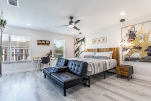 Ein modernes Schlafzimmer mit einem Bett, einer schwarzen Ledersofa, einem Schreibtisch und einem Deckenventilator.
